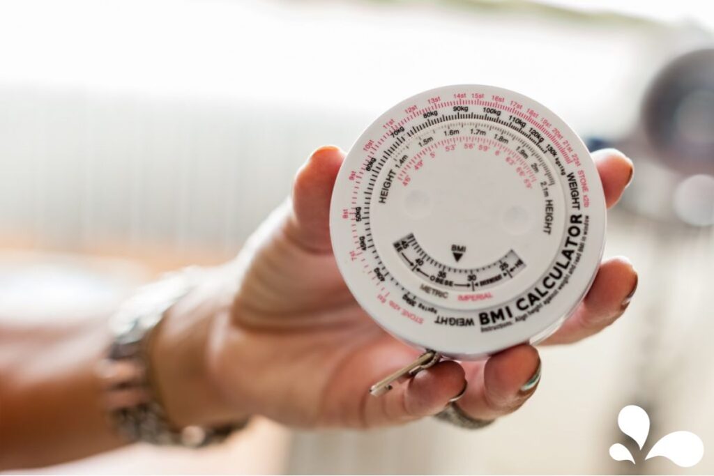 Close-up of a hand holding a BMI (Body Mass Index) wheel calculator, displaying various weight and height measurements in both metric and imperial units.