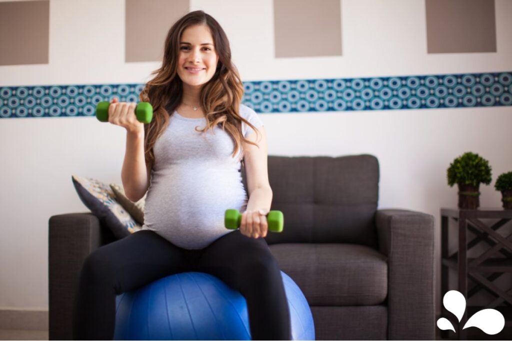 An expectant mother in casual workout attire using light dumbbells and a fitness ball, demonstrating safe pregnancy exercises.