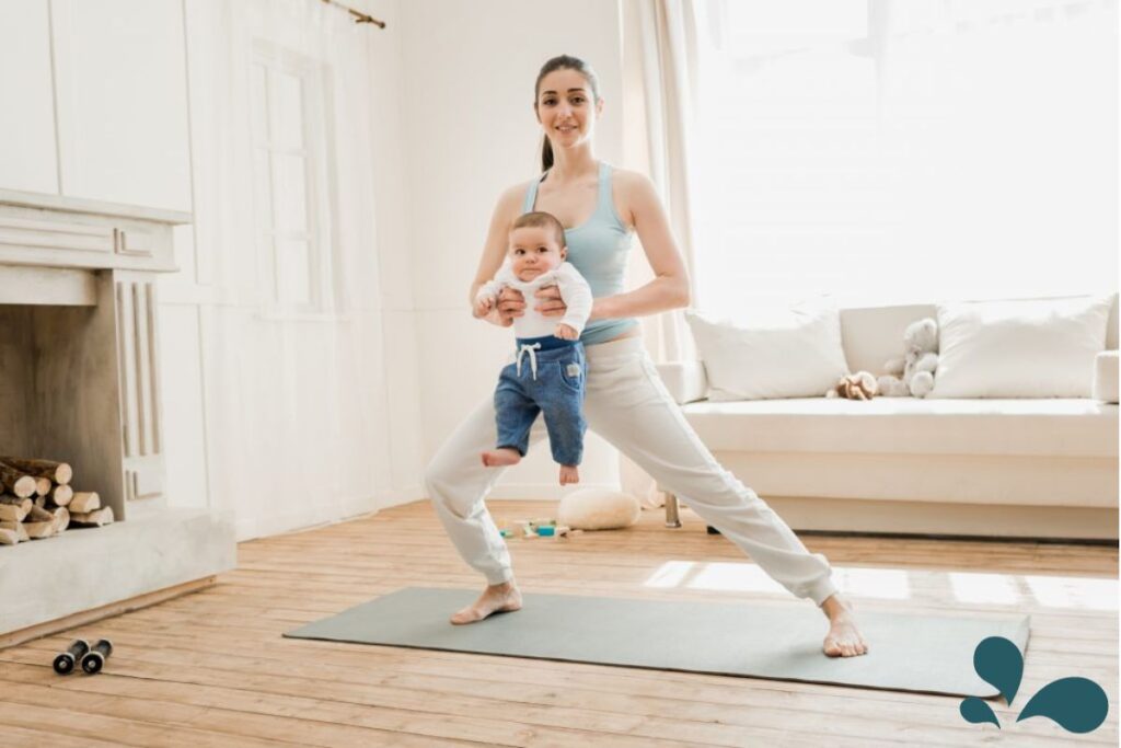 Mom exercising while holding her baby in a neutral color, decorated living space with natural light streaming in through the window.