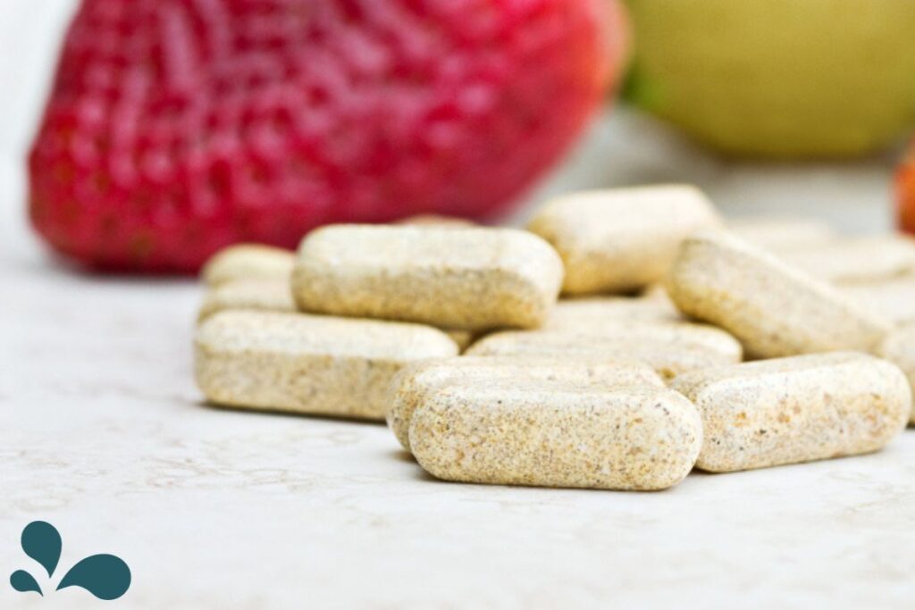 Close-up of prenatal vitamins on a marble countertop with blurred fresh fruits in the background, emphasizing the importance of supplements during pregnancy.