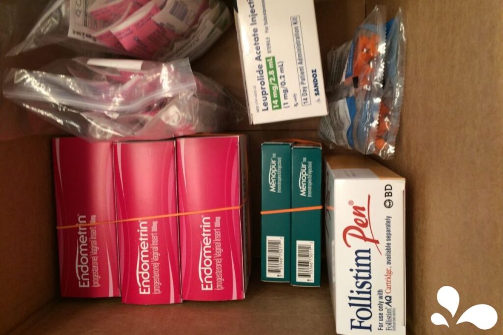 Various medications and medical supplies, including syringes and pharmaceutical boxes, arranged in a box for fertility treatment protocols.