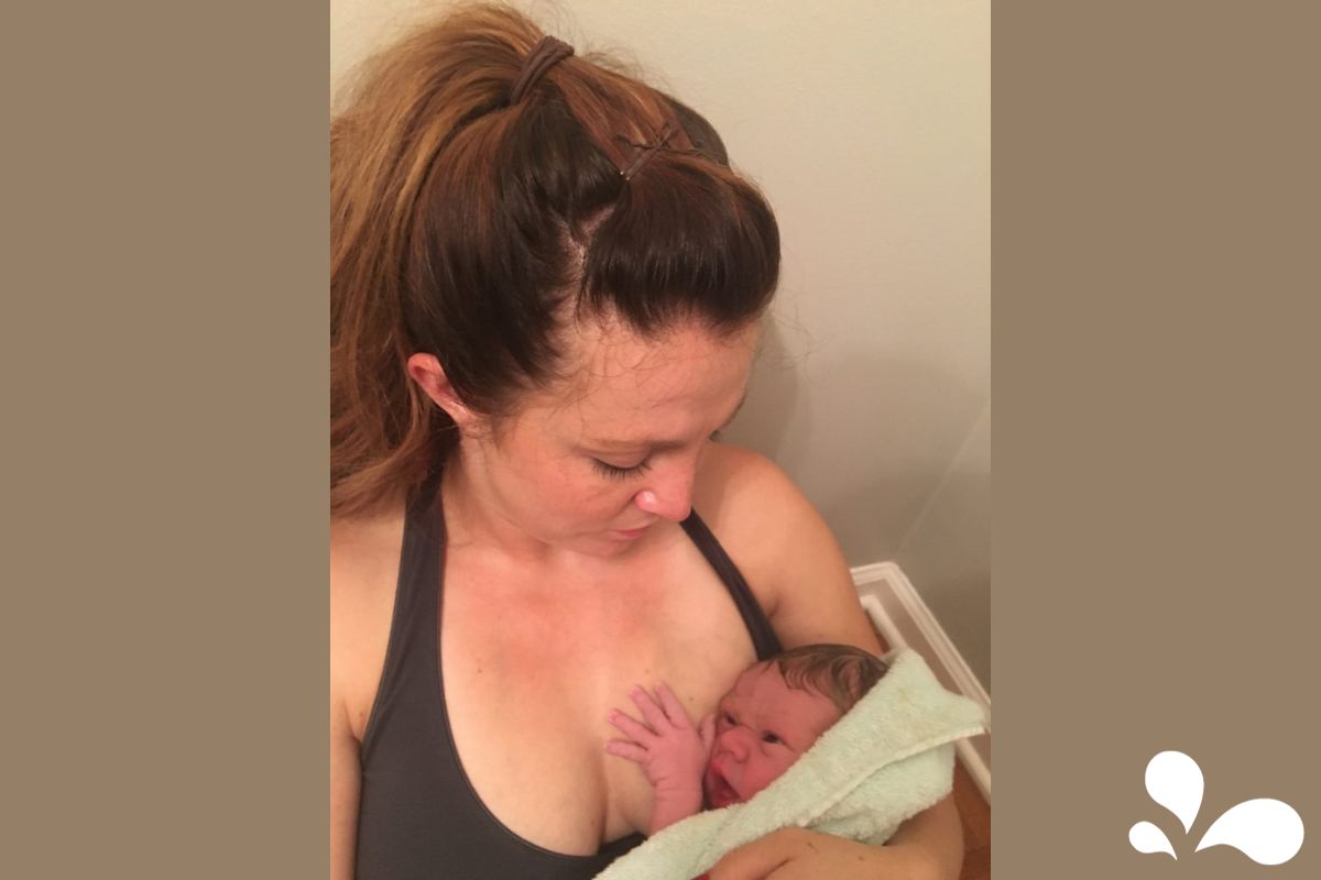 A heartwarming close-up of Jesi, a new mother with her hair up in a casual bun, holding her newborn baby, Tavin, after a bath. Tavin is wrapped snugly in a soft green towel, with one tiny hand reaching out. Both are in a serene bathroom setting, embodying a moment of peaceful connection and maternal love.