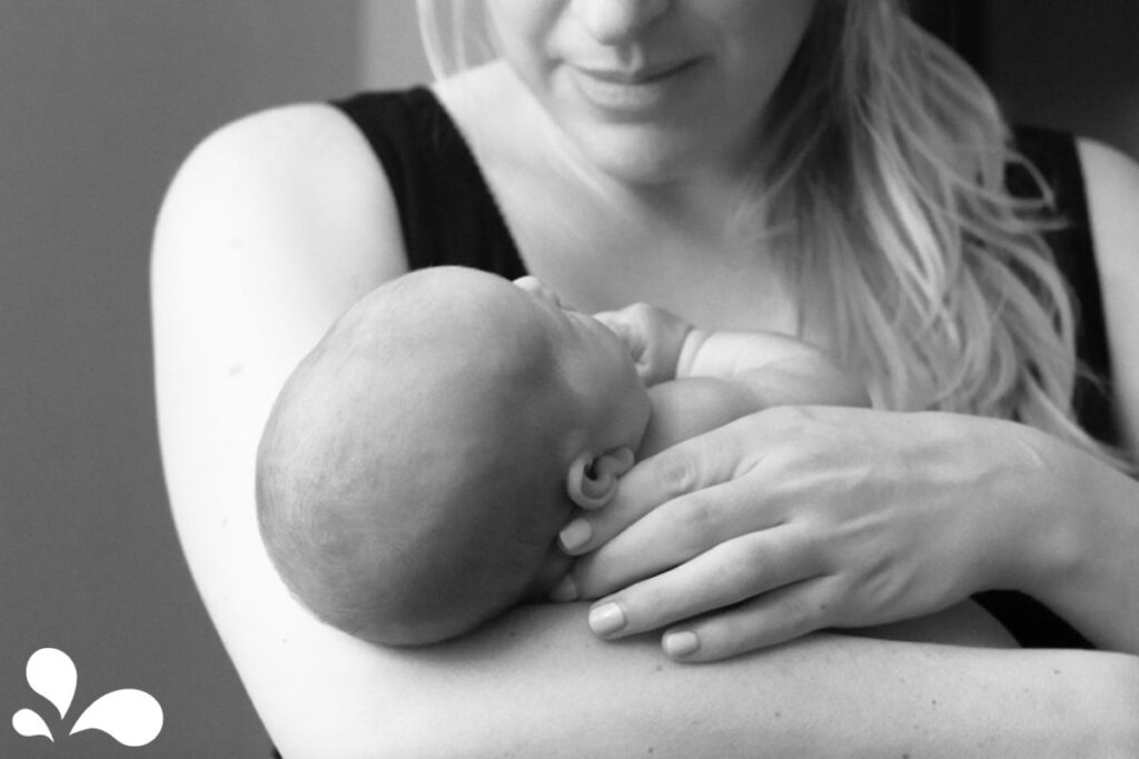 A black and white image capturing an intimate moment between a mother and her newborn. The mother, gently cradling her baby in her arms, looks down with affection as the baby rests against her. This picture exemplifies the close bond and tender connection that breastfeeding nurtures between mother and child.