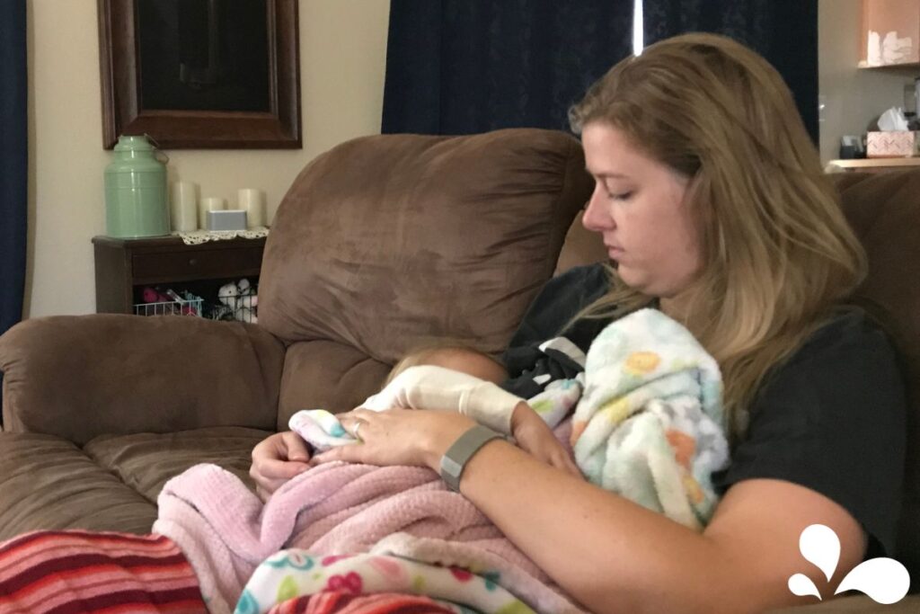 A mother sitting comfortably on a couch, looking down tenderly at her baby wrapped in a blanket while breastfeeding.