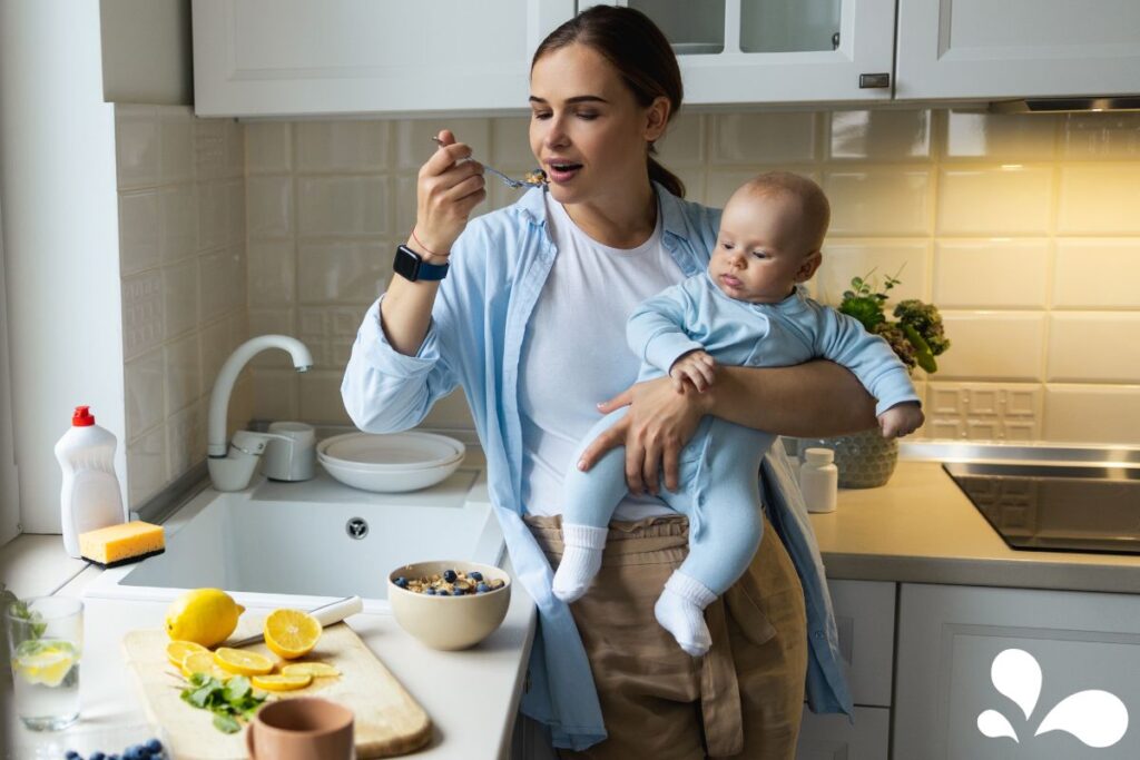 An image of a busy mother in a kitchen, tasting food while holding her baby on her hip. This picture portrays the multitasking nature of motherhood and the importance of maintaining a healthy diet to support breastfeeding.