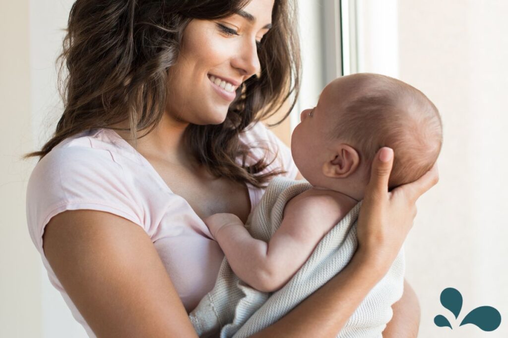 A smiling mother in a pink shirt holds her baby wrapped in a blanket, sharing a loving and intimate moment.