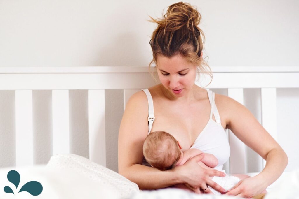 Detailed image of a woman in a white tank top, holding her chest with both hands, indicating the area of her plugged milk ducts.