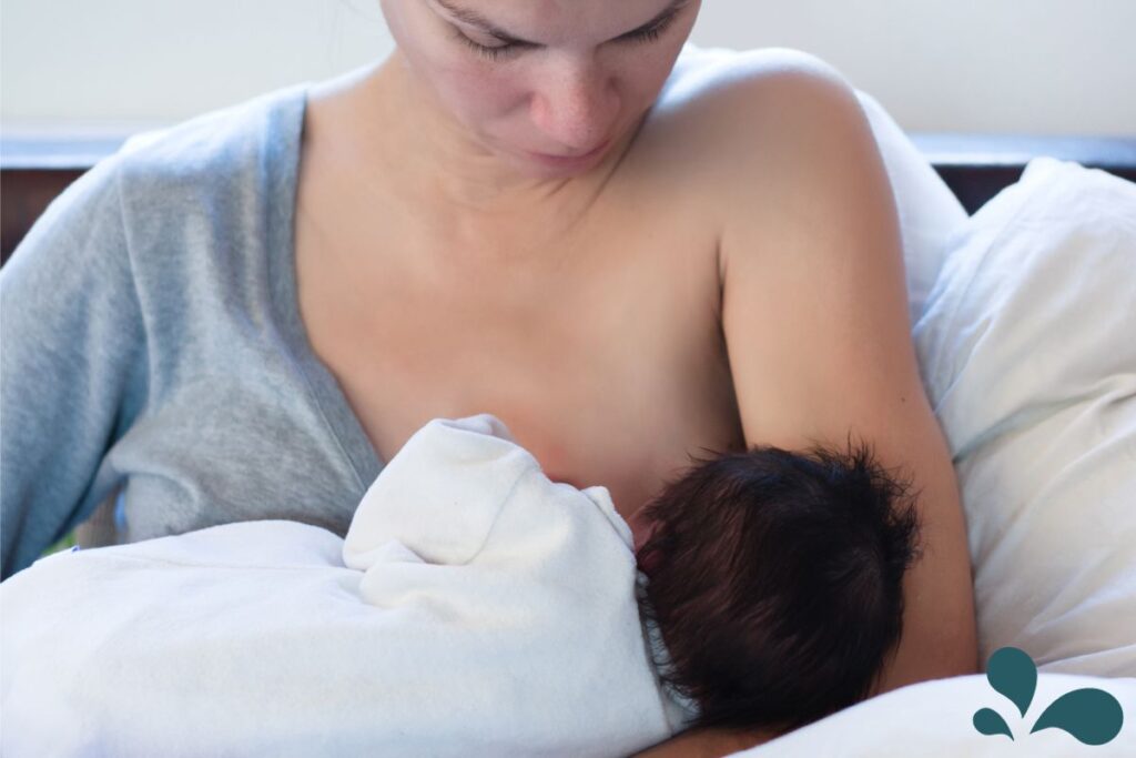 An image depicting a serene breastfeeding scene where a mother, in a relaxed pose, feeds her baby who is wrapped in a white cloth. The calm and focused expression on the mother's face highlights the peaceful and nurturing environment essential for breastfeeding.