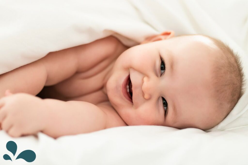 A content baby nestled in soft white blankets, giving a toothless grin and sparkling eyes full of joy.