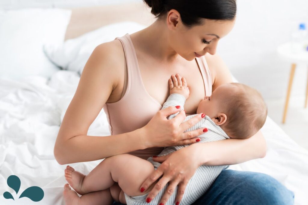 A mother seated at the end of a bed, lovingly breastfeeding her baby, highlighting the intimacy of the moment.