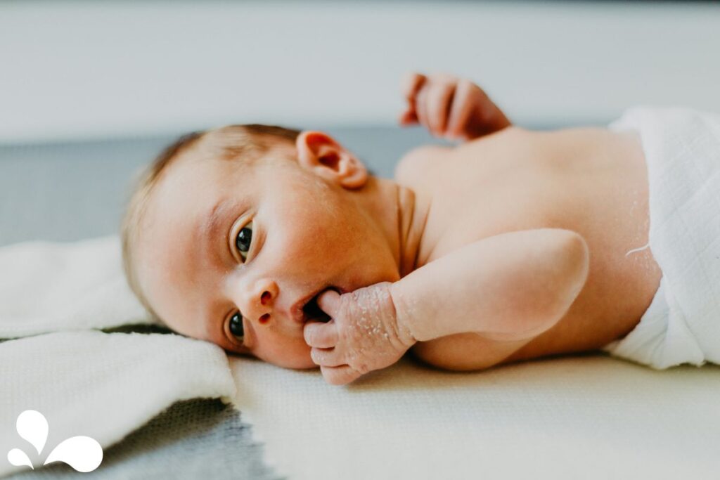 A calm baby bringing hands to their face, a behavior often associated with hunger and self-soothing.