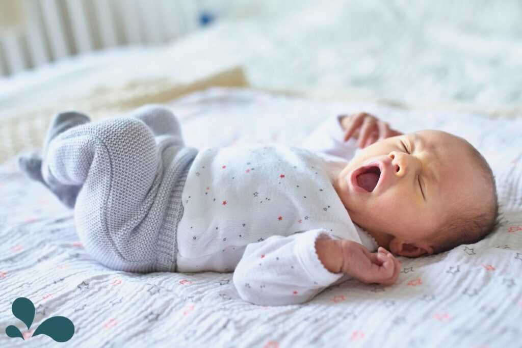 A baby lying comfortably on a soft blanket, opening their mouth wide as an early sign of hunger.