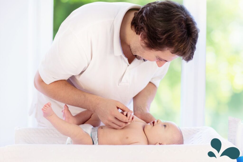 A father changing his baby's diaper on a changing table, demonstrating an active role in parenting and support.