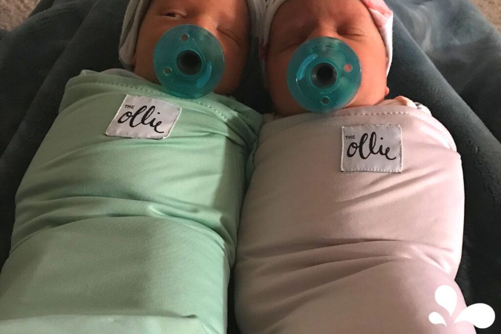 Two newborn twins swaddled in mint green, each with a pacifier, lying side by side.