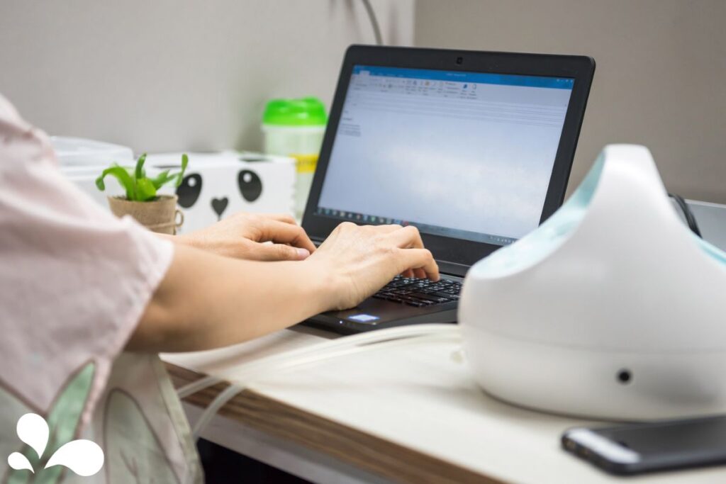 A mother is focused on her computer work while using a breast pump, showcasing the efficiency of combining work tasks with pumping milk.