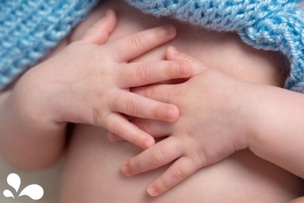 Close-up of a newborn's tiny hands resting gently on their chest, enveloped by a soft blue knitted blanket, depicting the calmness and innocence of early life.