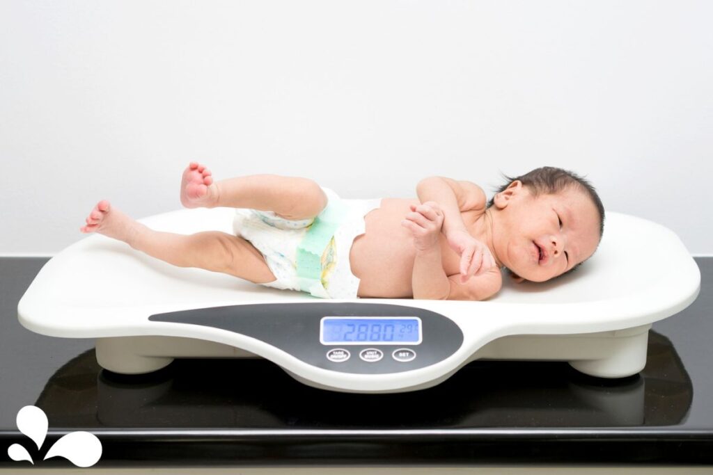 Check the weight of a newborn baby using a scale with a white wall background.