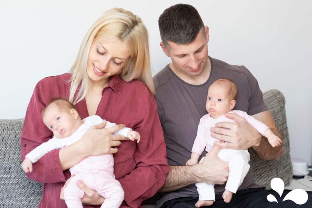 A mother and father each holding a newborn twin, smiling and enjoying their first moments as a larger family.
