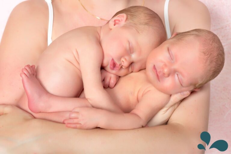 Newborn twins sleeping soundly while nestled together in their mother's arms, symbolizing the bond between multiples.