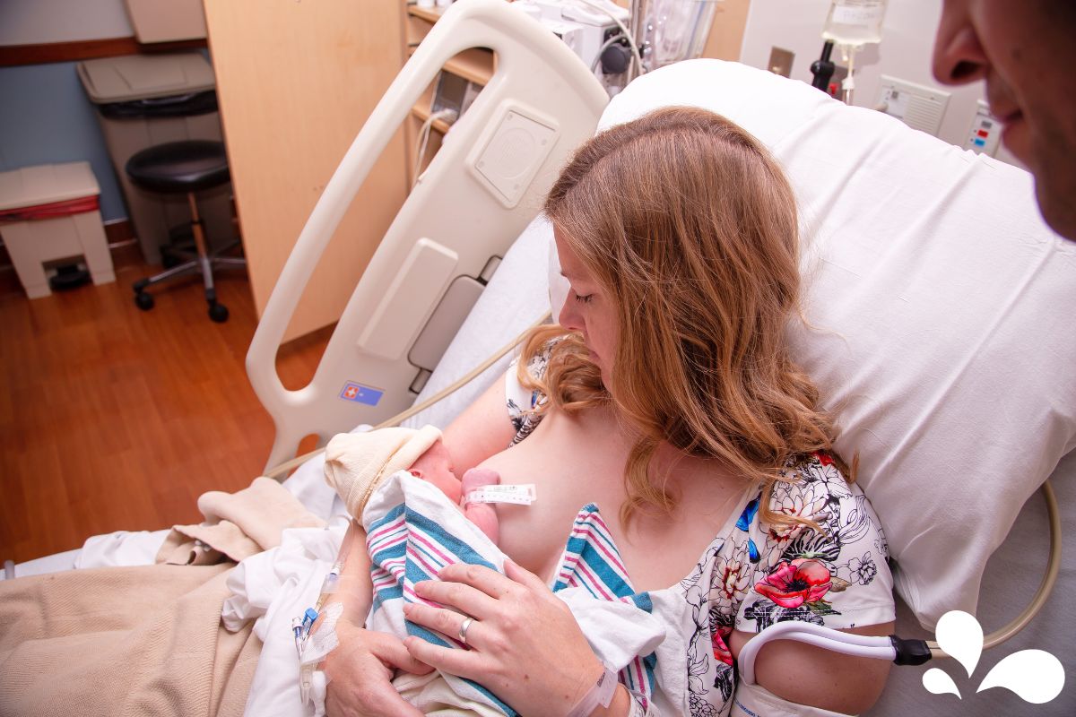 A new mother in a hospital bed lovingly holds her newborn baby close for skin-to-skin contact, cherishing the first moments of connection.