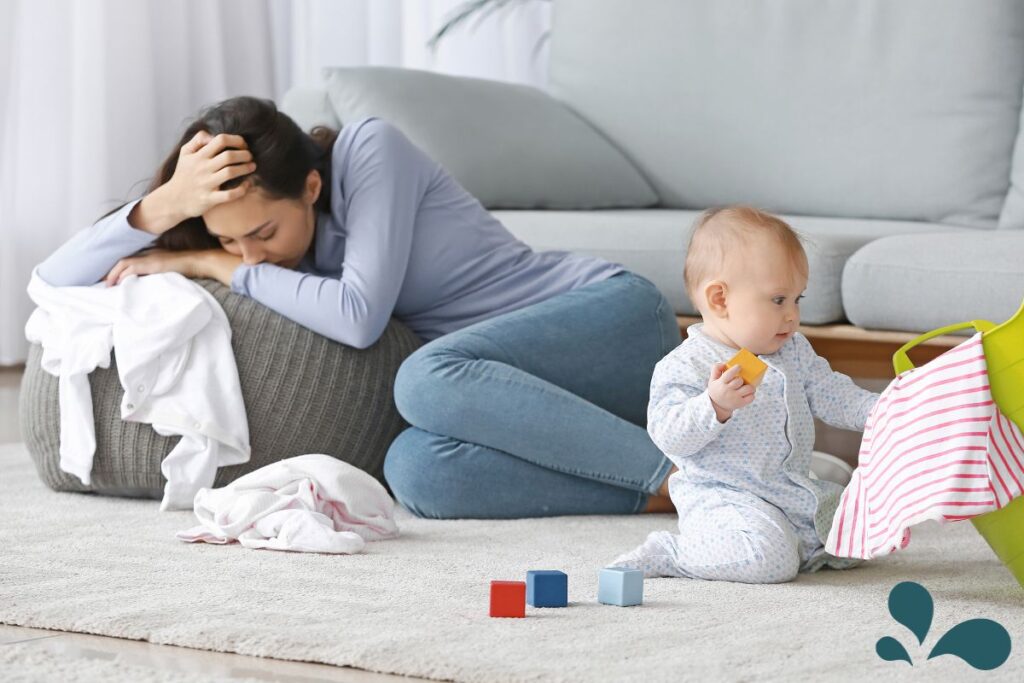 A distressed mother with a baby playing nearby, depicting the unseen struggles of postpartum depression amidst daily life.