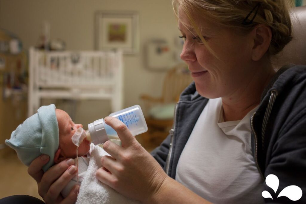A devoted mother in a hospital NICU tenderly bottle-feeding her premature baby, providing essential nutrients and a loving touch.