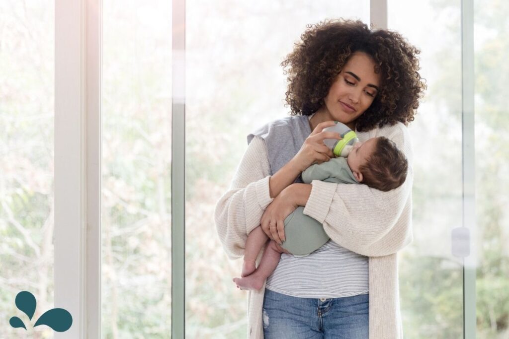 A mother standing by a window, lovingly bottle-feeding her baby, capturing a serene moment of motherhood.