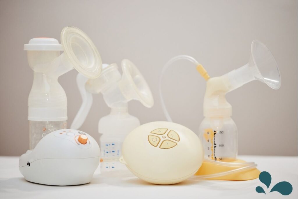 A variety of breast pumps on a white surface, showcasing different models and styles, including manual and electric pumps with transparent flanges and collection bottles. The equipment is designed for expressing and collecting breast milk, depicted in a clean and minimalist setting.