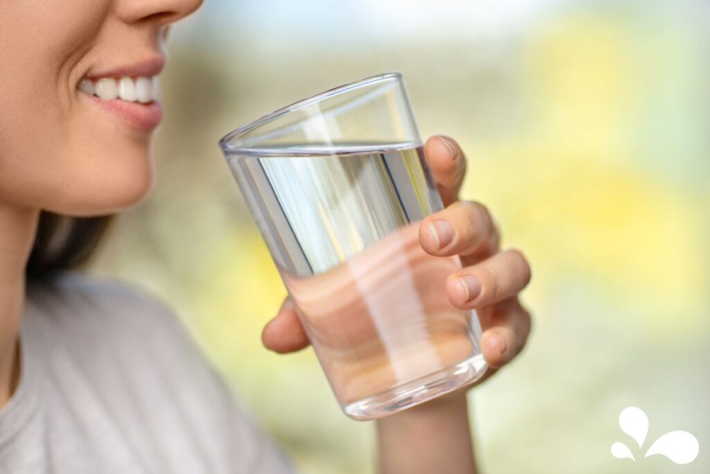 Close-up of a smiling woman about to drink from a clear glass of water, highlighting the importance of hydration for health.