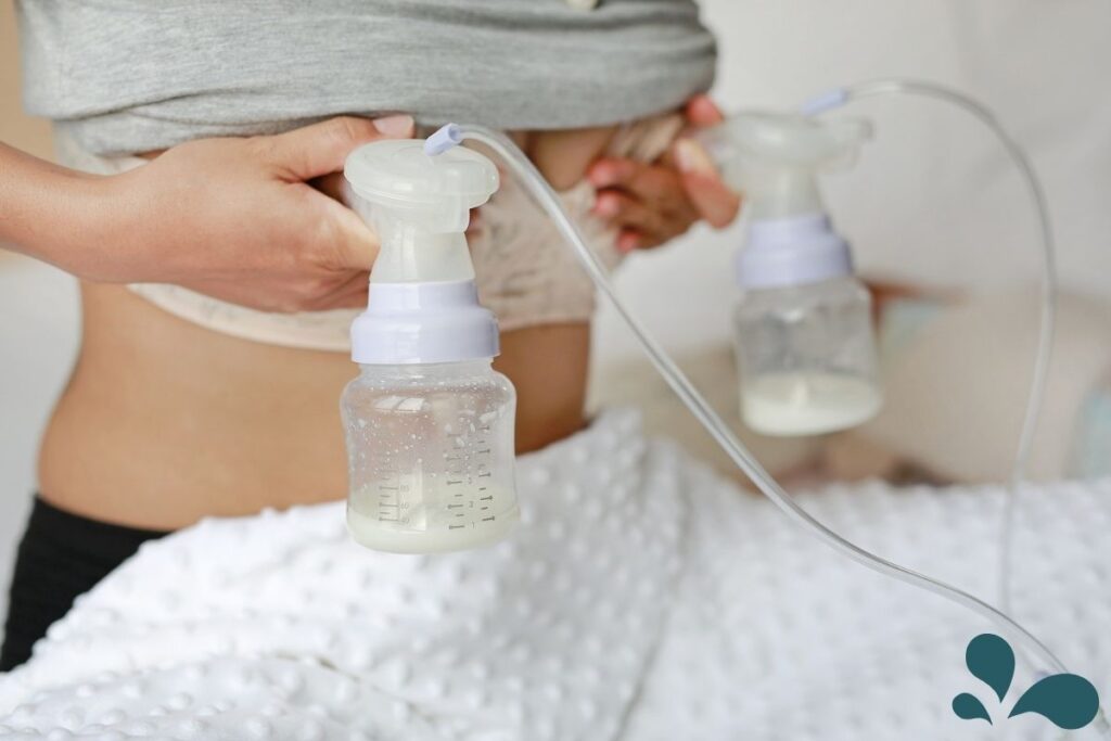 A mother is using a double electric breast pump, with bottles collecting breast milk. The focus is on the bottles and pump flanges attached to her, with a blurred background emphasizing the pumping process.