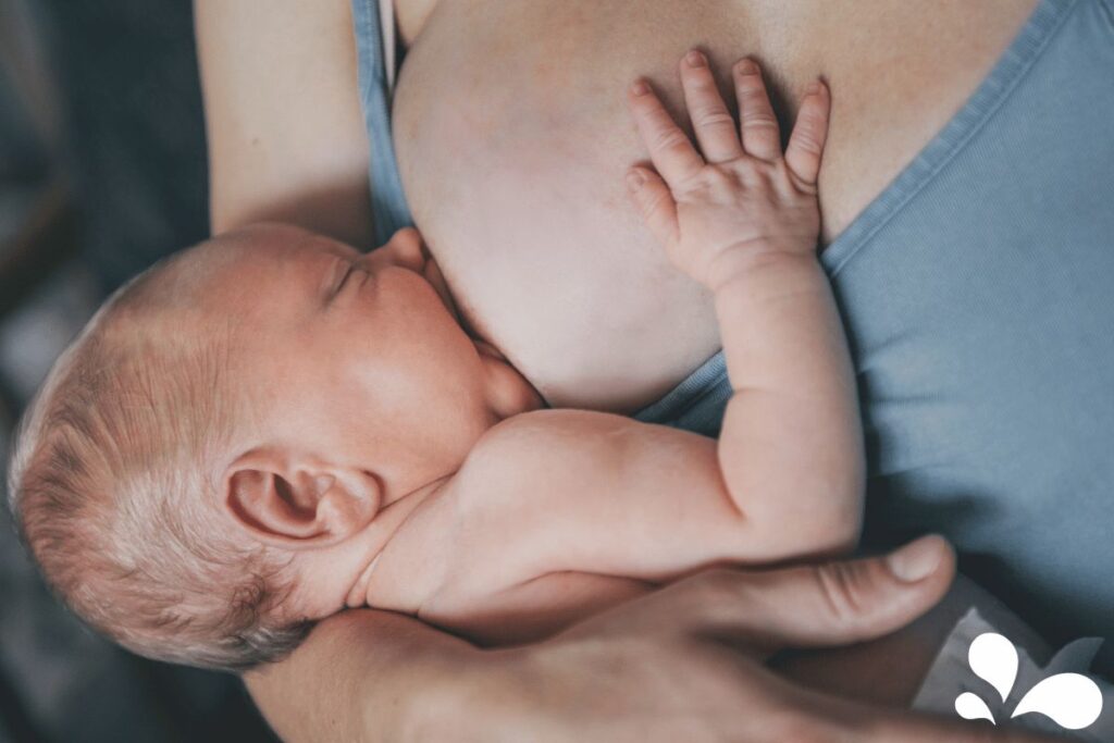 Close-up of a newborn with a deep latch while breastfeeding, showing the baby's ear, cheek, and hand gently touching the mother's breast.