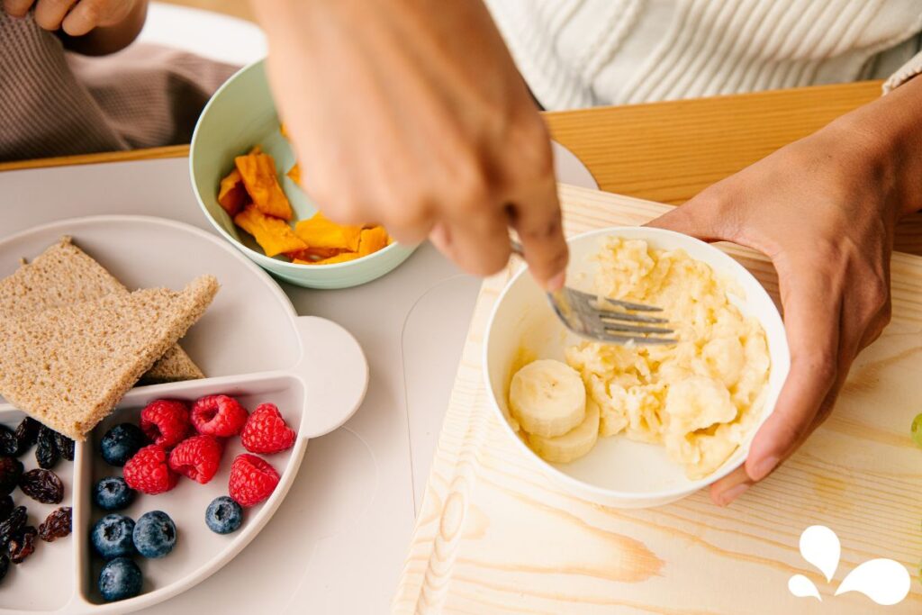 A hand mashing bananas on a wooden plate, preparing simple and nutritious baby food at home.
