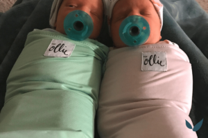 newborn twins on mothers lap wrapped in Ollie Velcro swaddles