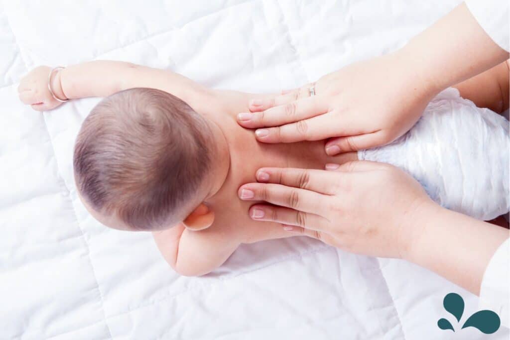 A baby receiving infant massage from back strokes.