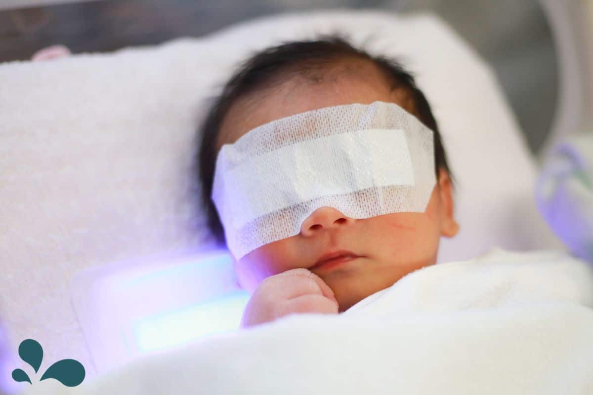 Newborn with eye covers laying on a bilirubin light blanket.