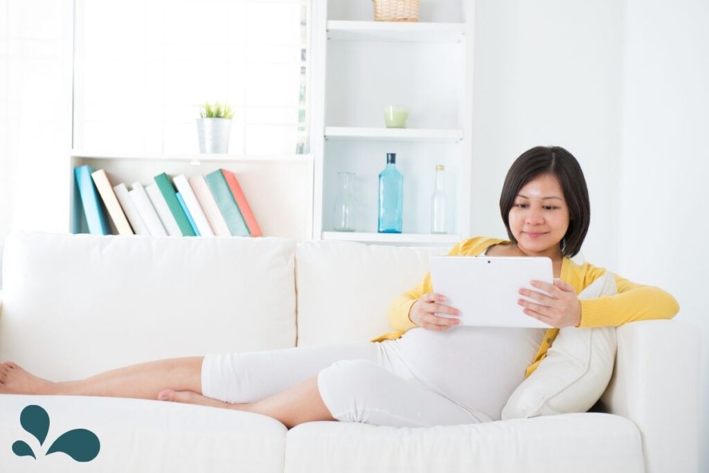A pregnant woman sitting a couch with a tablet