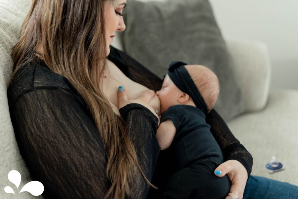 Close-up of a mother breastfeeding her baby dressed in black. The baby, wearing a headband, is latched onto the breast as the mother supports them in a nurturing embrace.